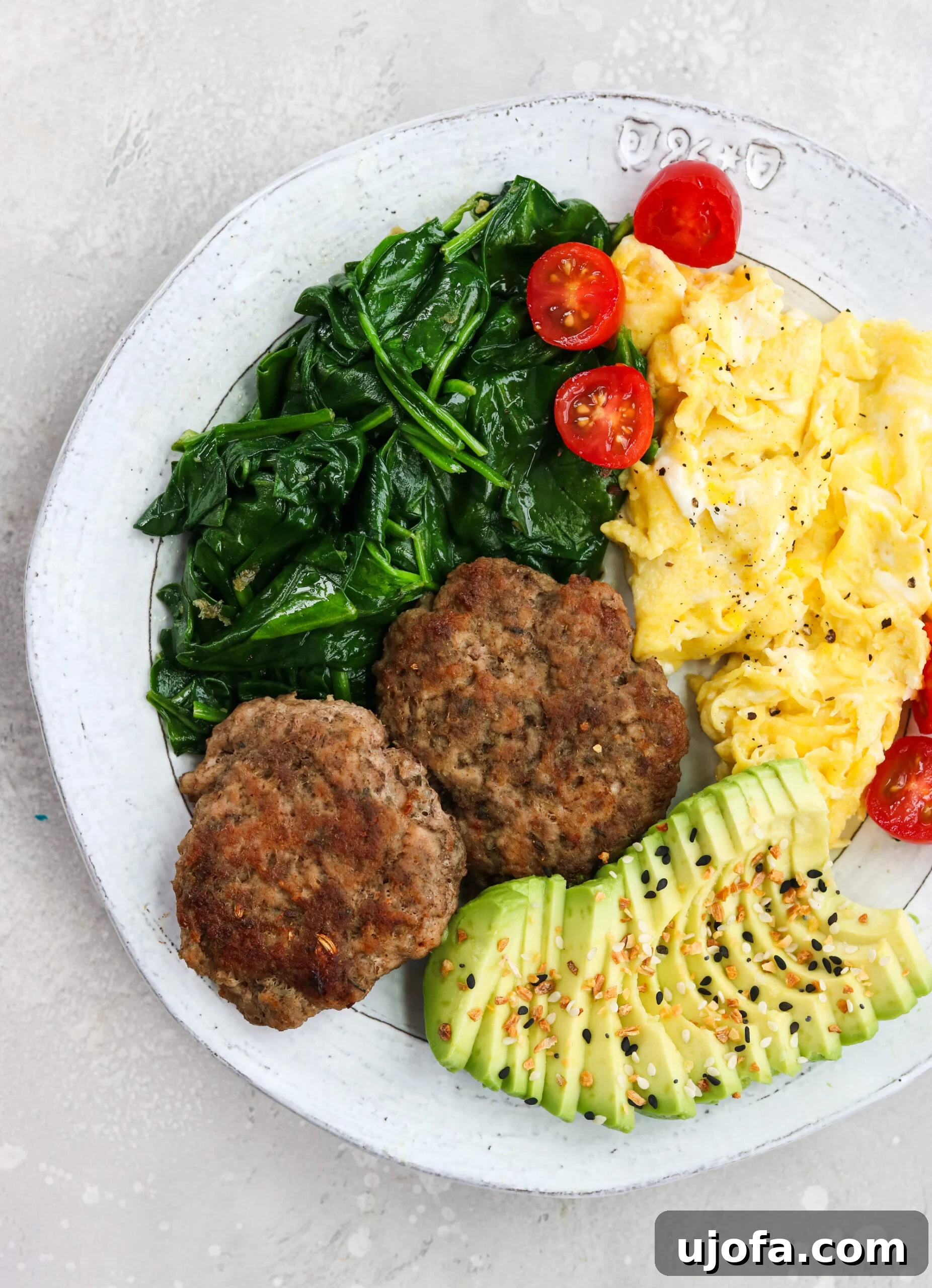 A hearty breakfast plate featuring golden-brown Air Fryer sausage patties, sautéed spinach, perfectly scrambled eggs, and fresh tomatoes.