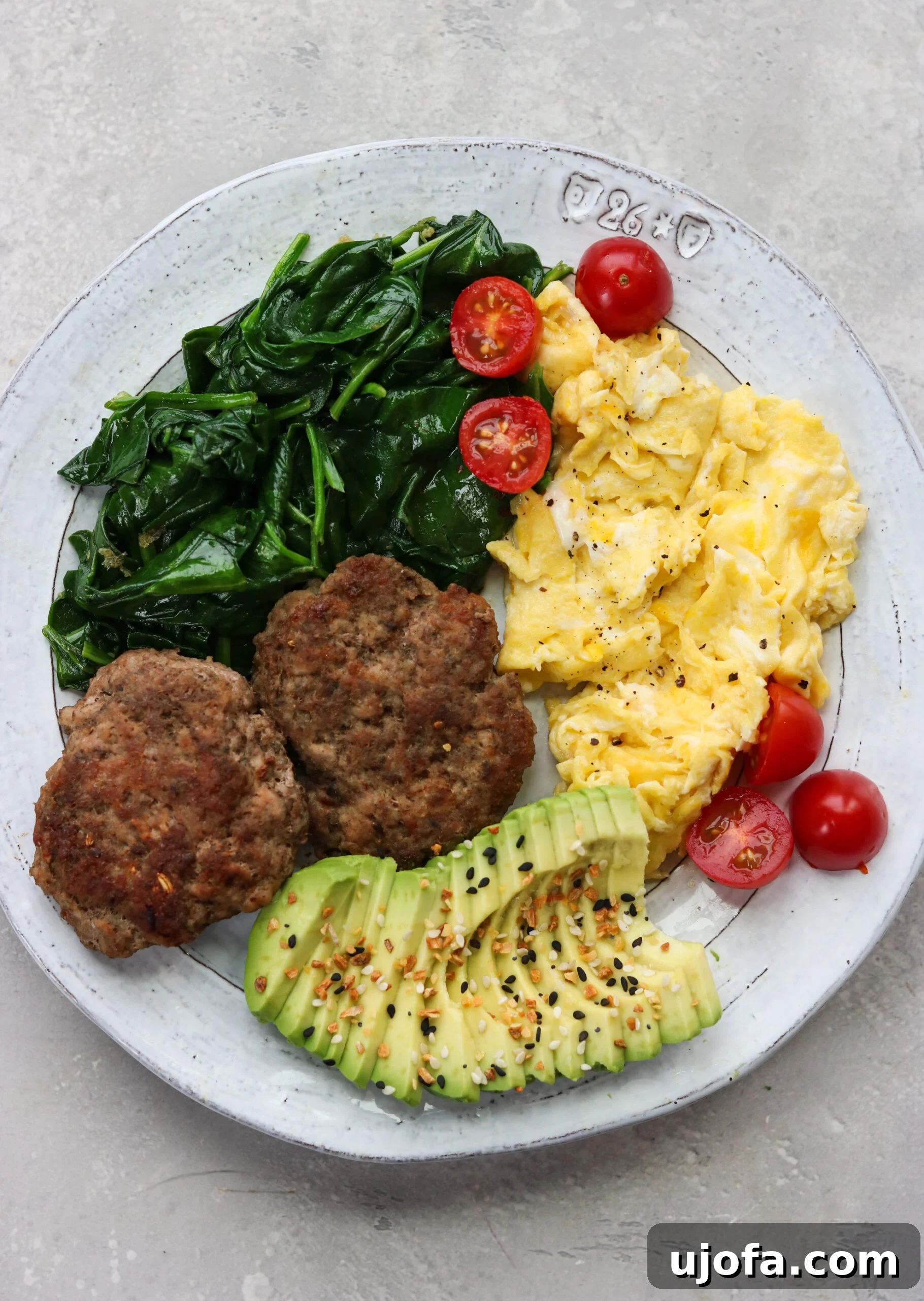 A balanced breakfast plate featuring homemade sausage patties, creamy avocado slices, perfectly cooked eggs, and fresh spinach, all seasoned with everything bagel seasoning.