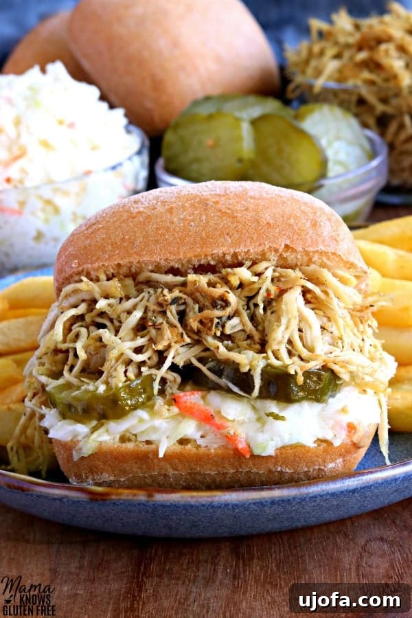 Delicious shredded chicken sandwich with coleslaw and pickles on ciabatta bread, served with a side of golden French fries.