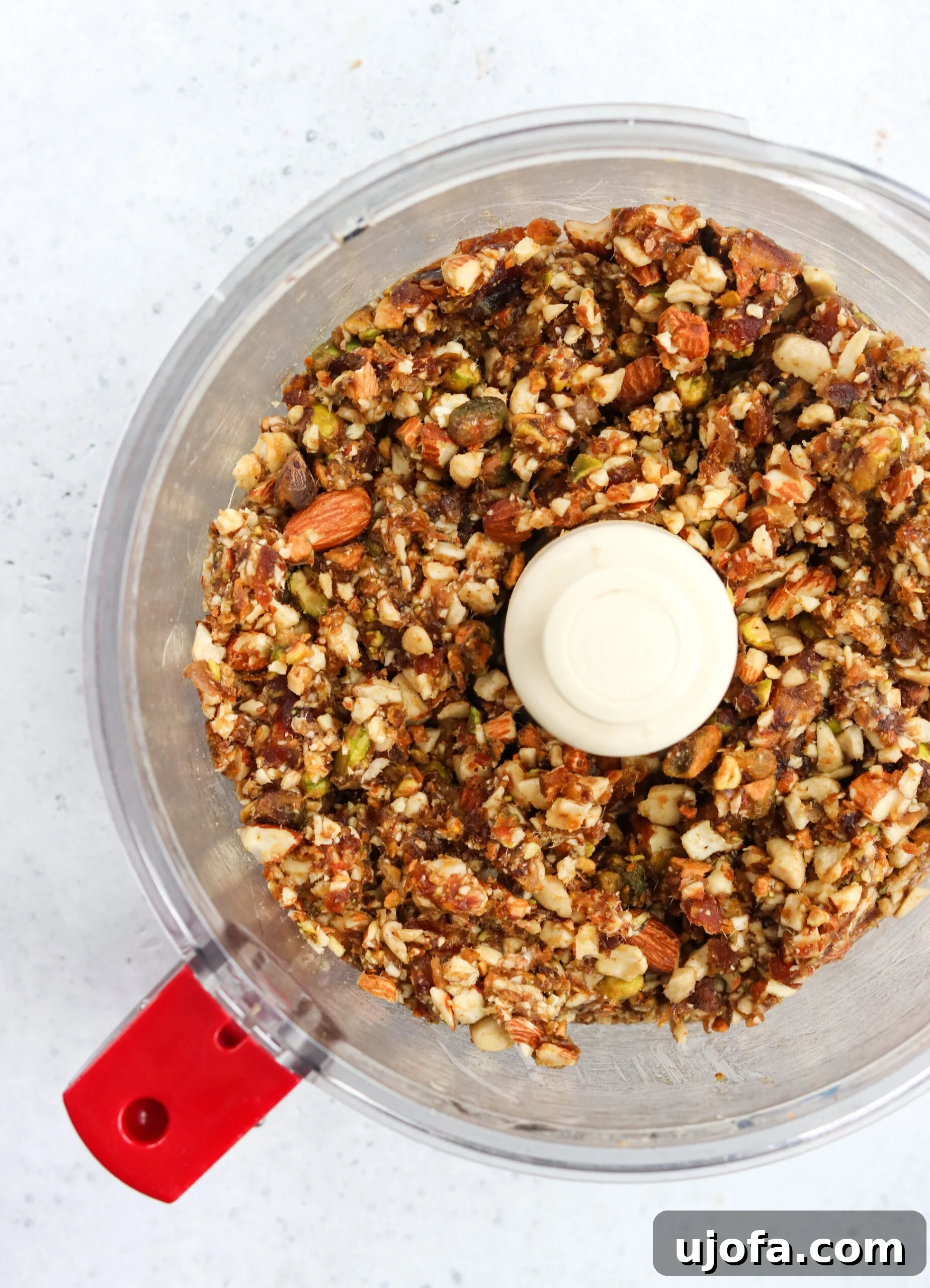 Mixed Nuts and Dates in Food Processor A food processor filled with a mixture of pitted dates and various nuts, ready to be pulsed into the bar base.