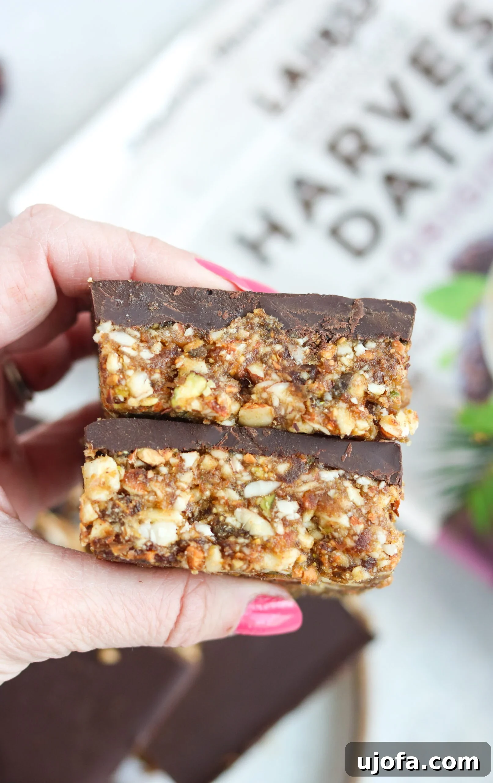 Woman Holding Chocolate Date Nut Bars A woman holding a delicious-looking Paleo Fudge Covered Date Nut Bar, showcasing the thick chocolate layer and nutty base.