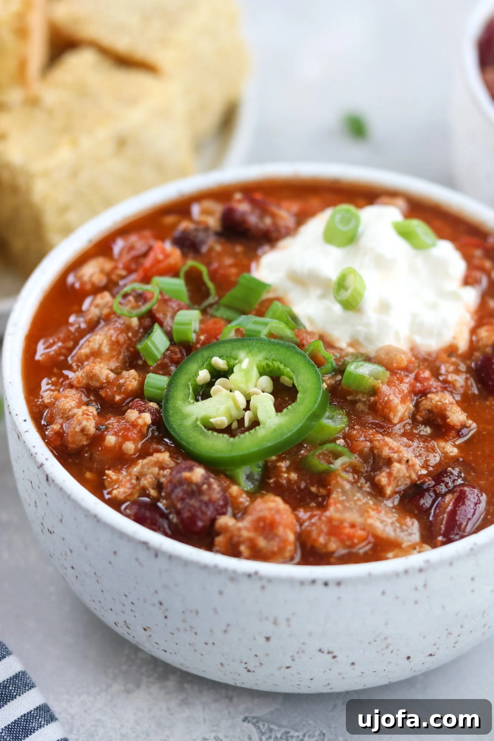 A closer look at the rich and chunky texture of slow cooker turkey chili, showcasing well-browned turkey, beans, and tomatoes, garnished with a green jalapeño slice.
