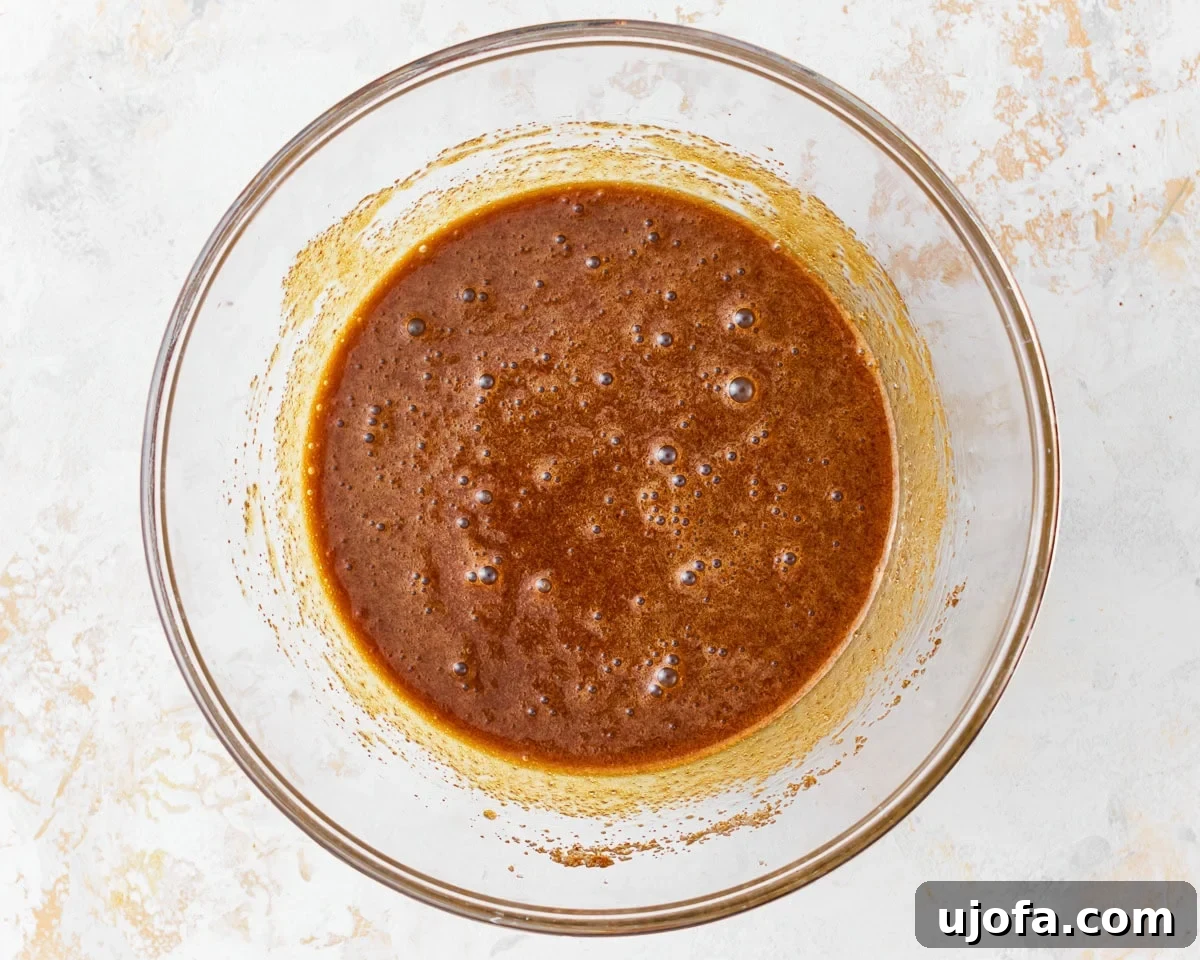 Wholesome Gluten-Free Pumpkin Delights 8 Brown sugar, granulated sugar, and oil mixed together for gluten-free pumpkin muffins in a glass mixing bowl, creating a smooth wet base.