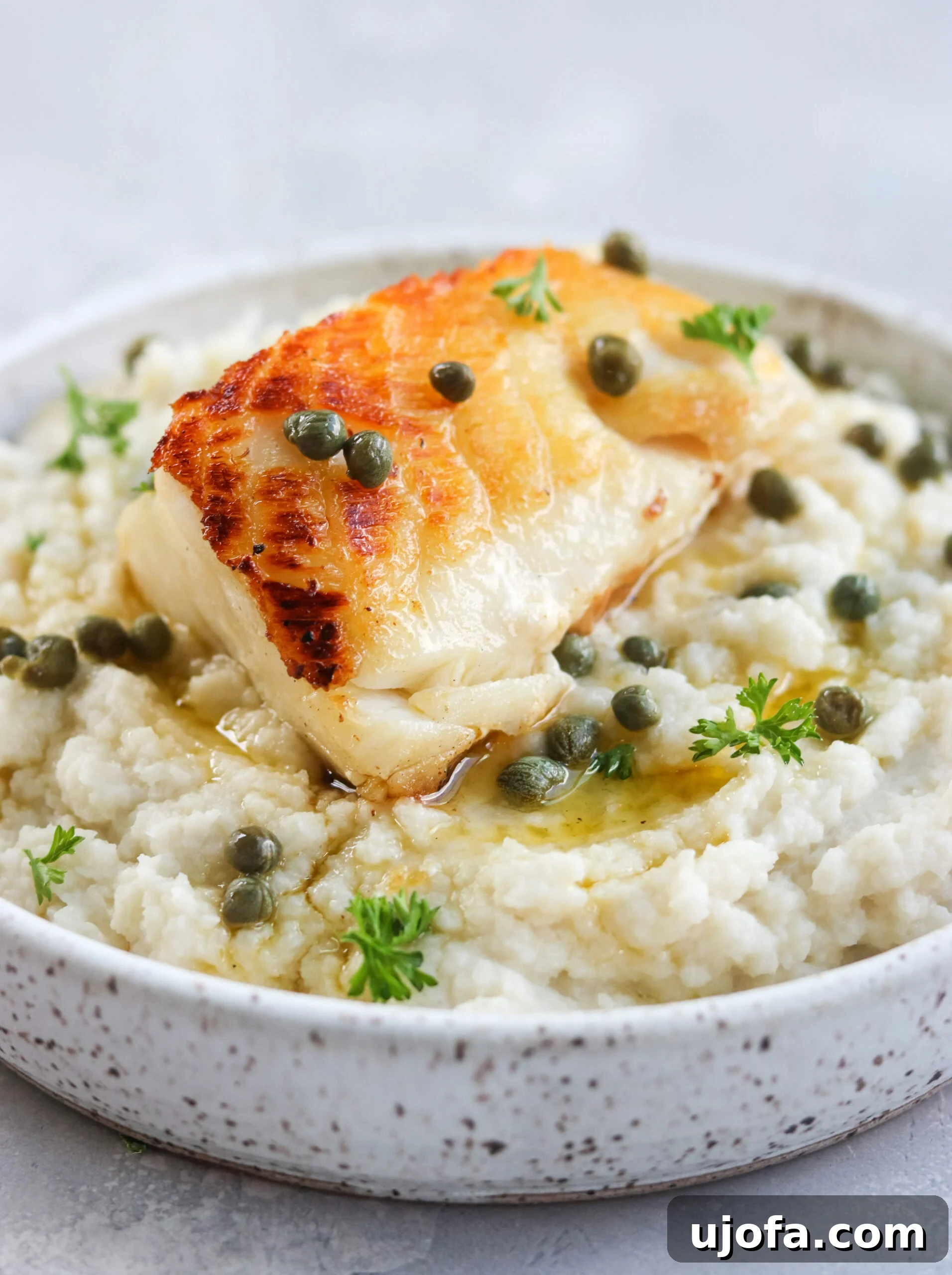 Pan Seared Chilean Sea Bass with Lemon Caper Butter on a serving dish Pan Seared Chilean Sea Bass with Lemon Caper Butter artfully arranged on a pristine white serving dish, garnished with fresh herbs.