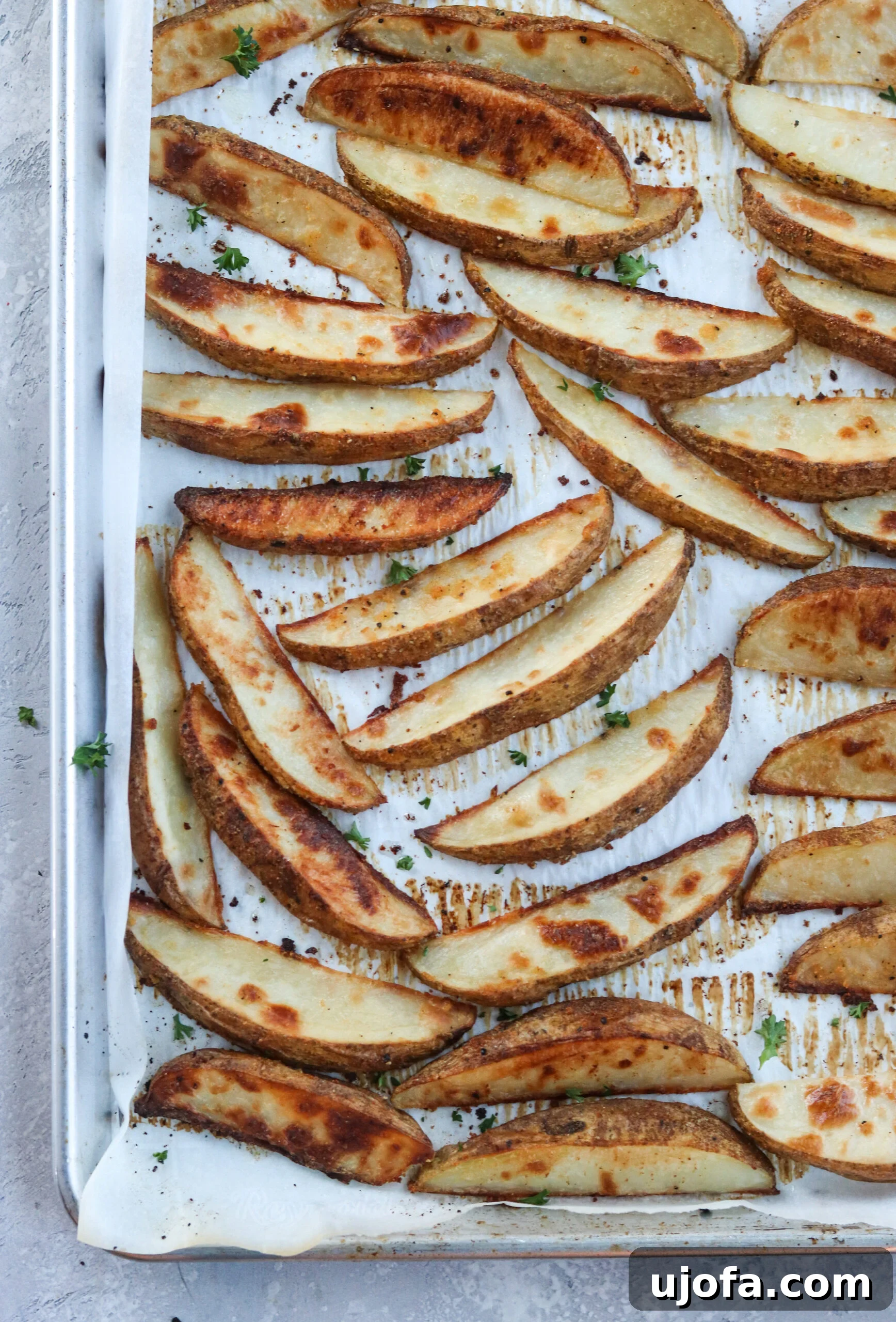 Crispy Baked Potato Wedges on a pan with parchment paper, fresh out of the oven, highlighting their golden brown and crispy texture