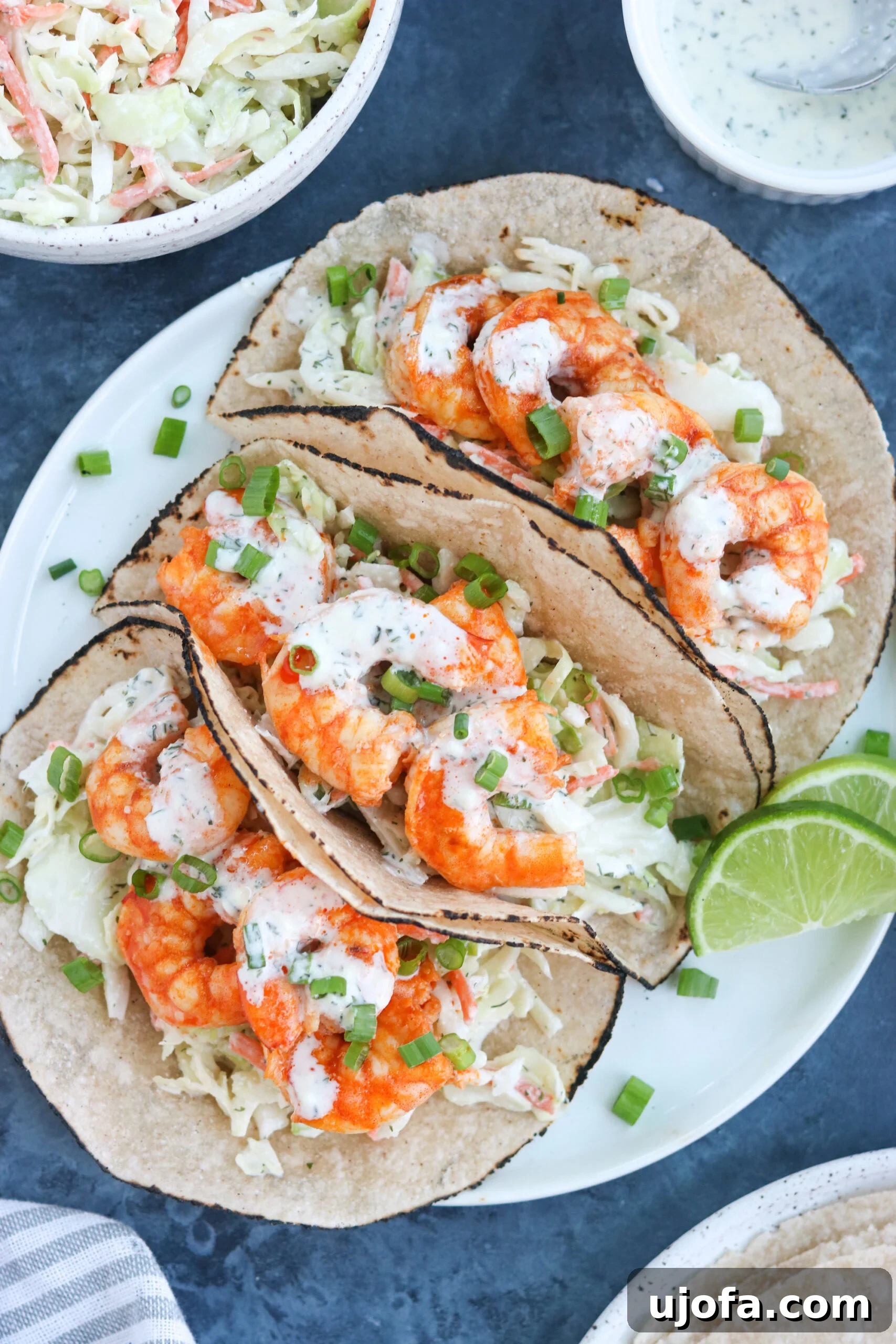 Three perfectly assembled Paleo Buffalo Shrimp Tacos on a white plate, garnished with a lemon wedge, ready to be enjoyed.