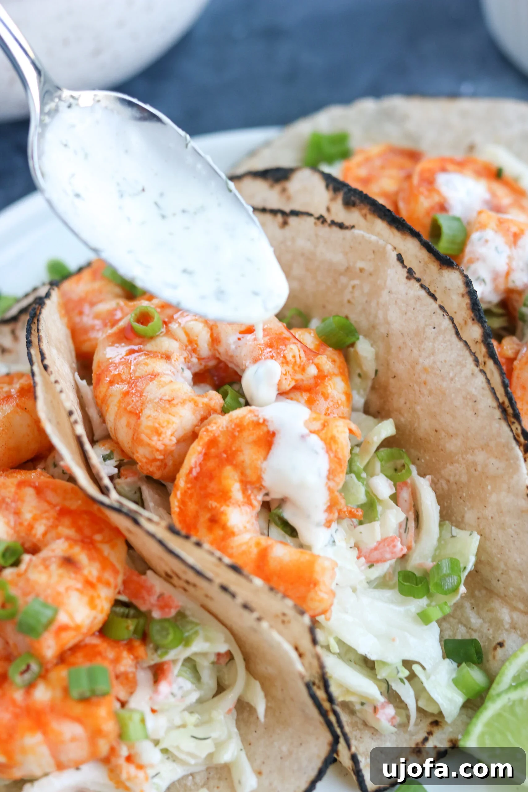 A spoon meticulously drizzles creamy sauce over a mouth-watering Paleo Buffalo Shrimp Taco, highlighting the fresh ingredients.