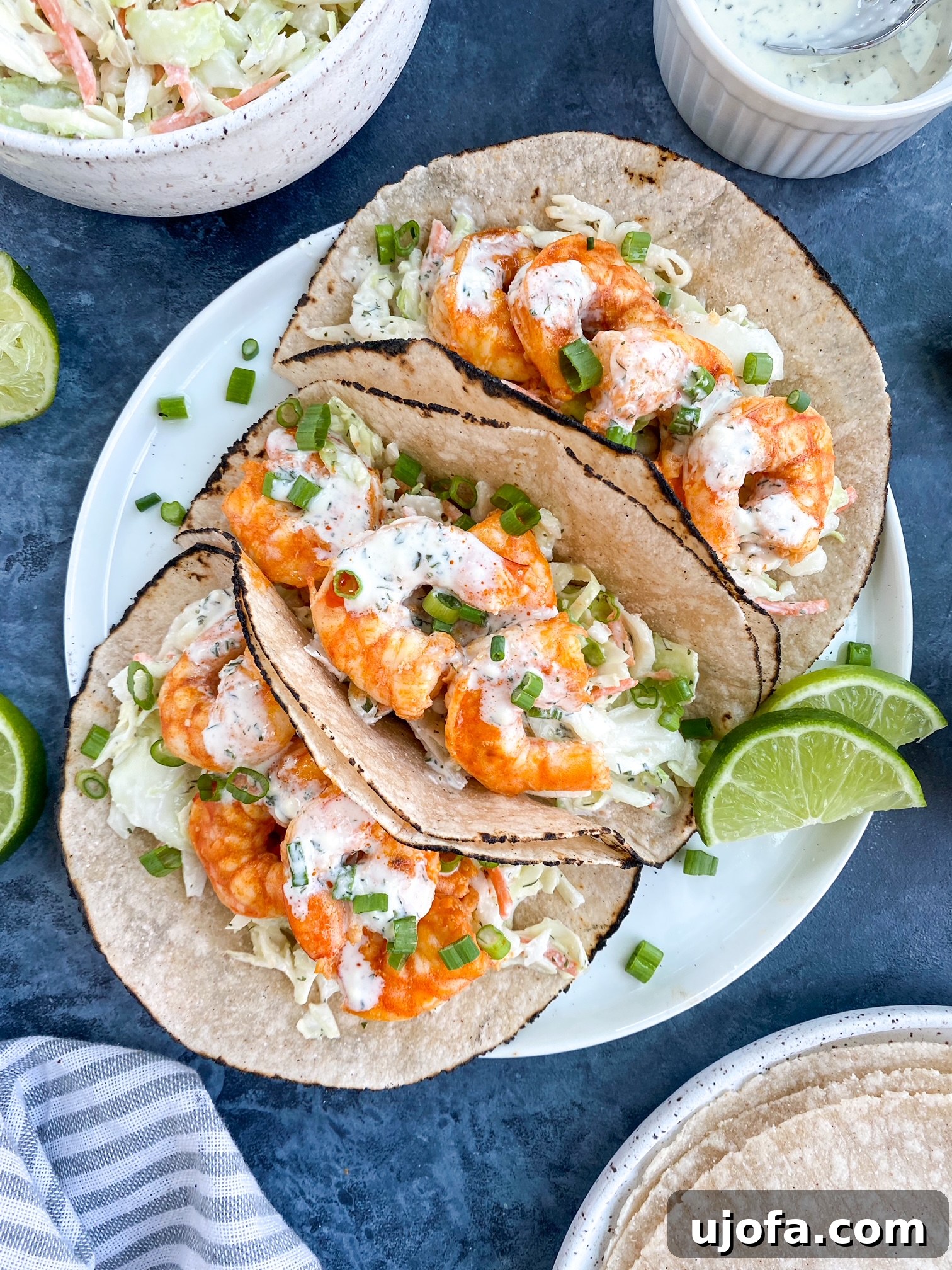 A close-up shot of three Paleo Buffalo Shrimp Tacos arranged neatly on a white plate, showcasing their vibrant fillings.