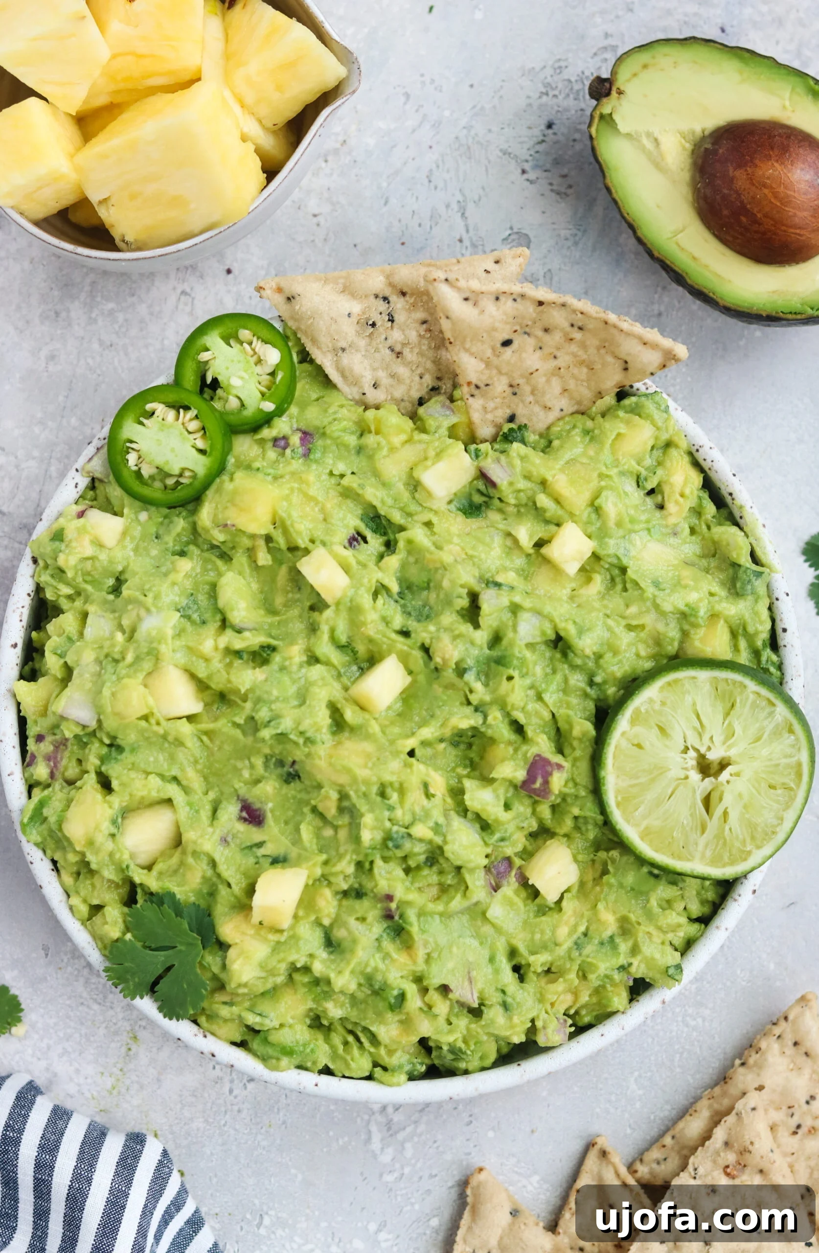 Bright green Paleo Pineapple Guacamole in a bowl, garnished with cilantro and surrounded by fresh pineapple and avocado slices, ready to be served with grain-free chips.