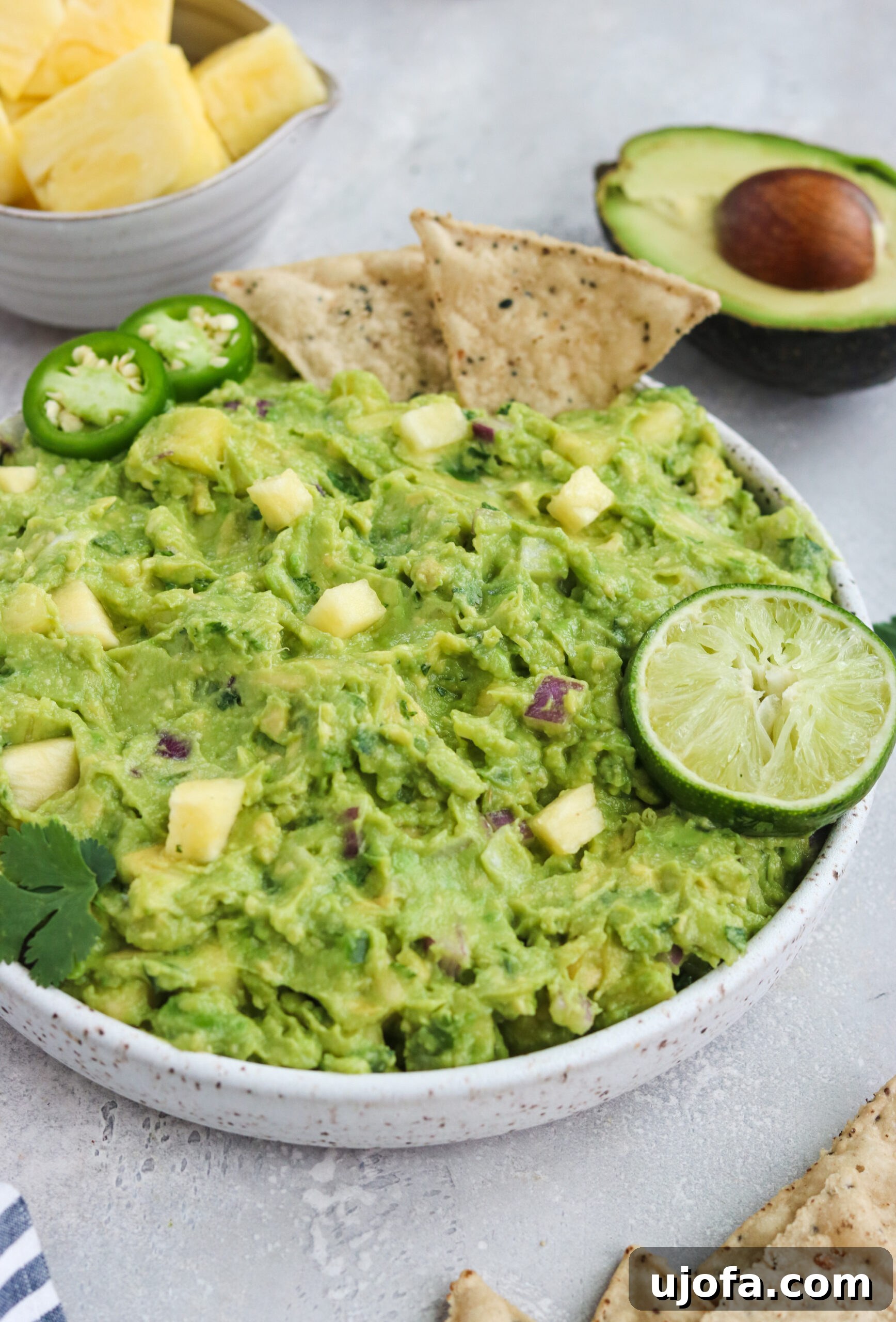 Close-up of a bowl of Paleo Pineapple Guacamole, showing chunks of avocado and pineapple, with a whole avocado and lime in the background.