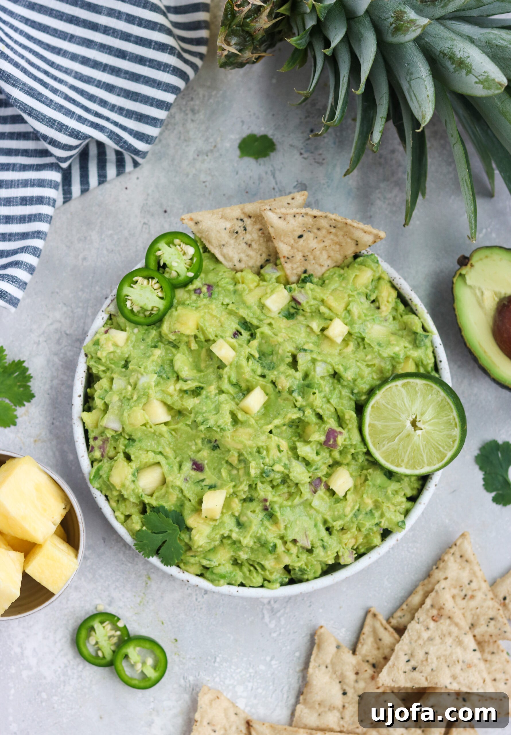 A vibrant bowl of Paleo Pineapple Guacamole with fresh lime and colorful tortilla chips on the side, ready for dipping.