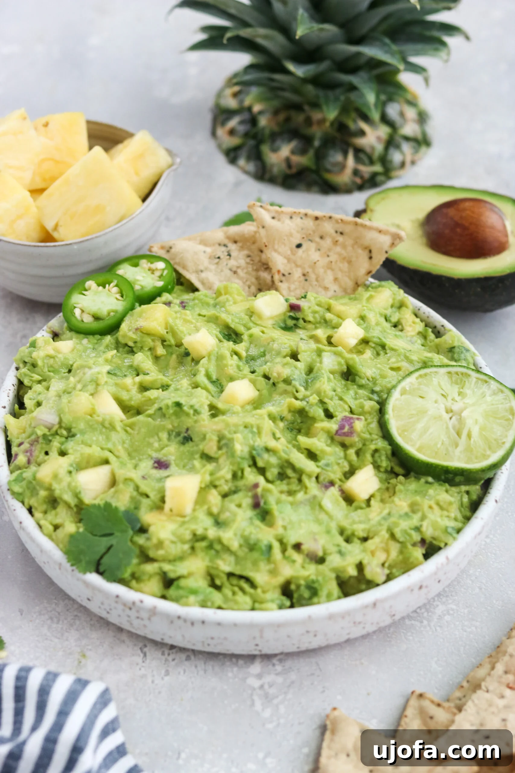 Overhead shot of a bowl filled with Paleo Pineapple Guacamole, showing the colorful mix of ingredients, alongside a serving spoon and fresh lime halves.