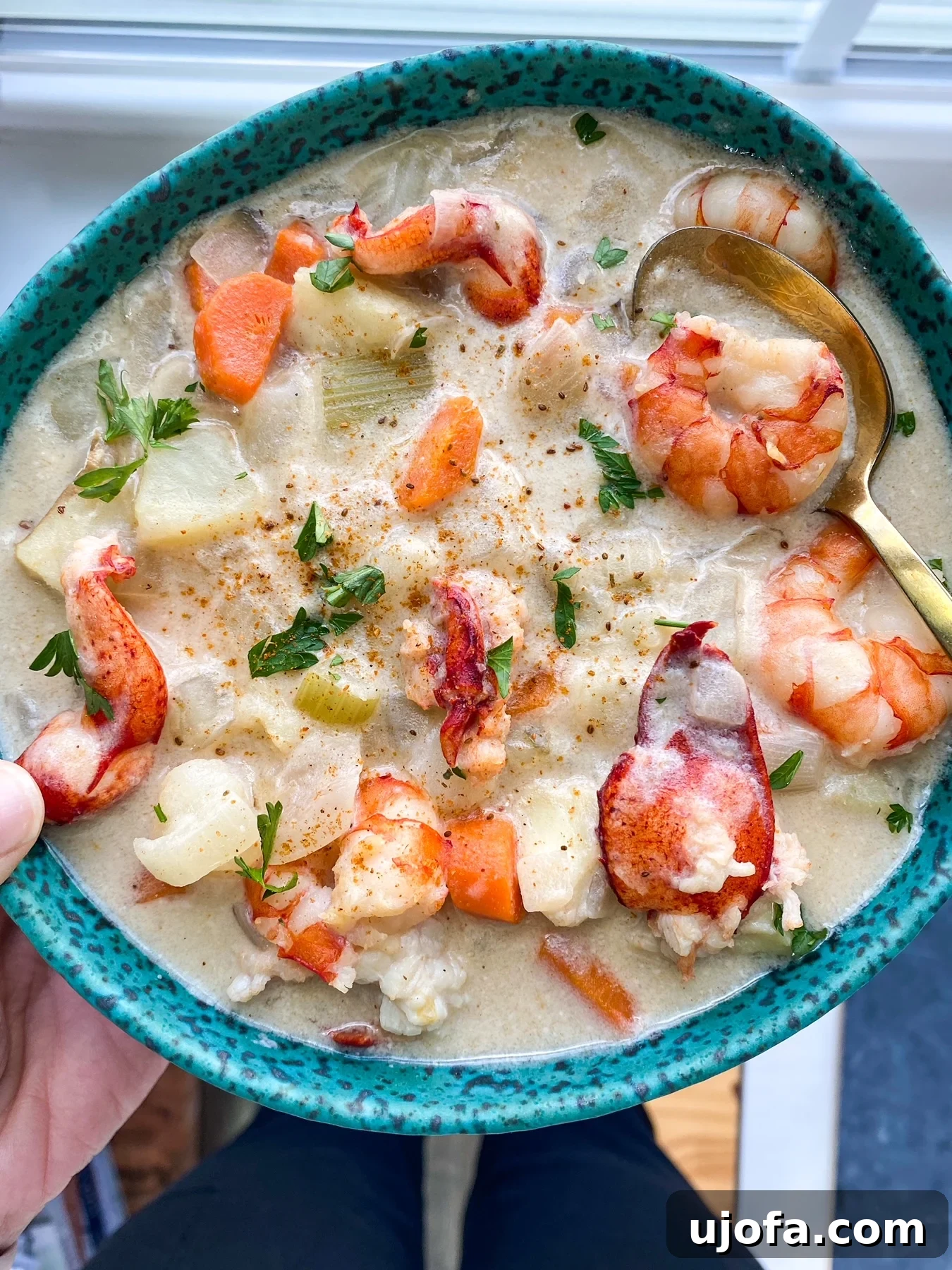 Hearty Paleo Seafood Chowder A close-up of a golden spoon scooping creamy seafood chowder from a bowl.
