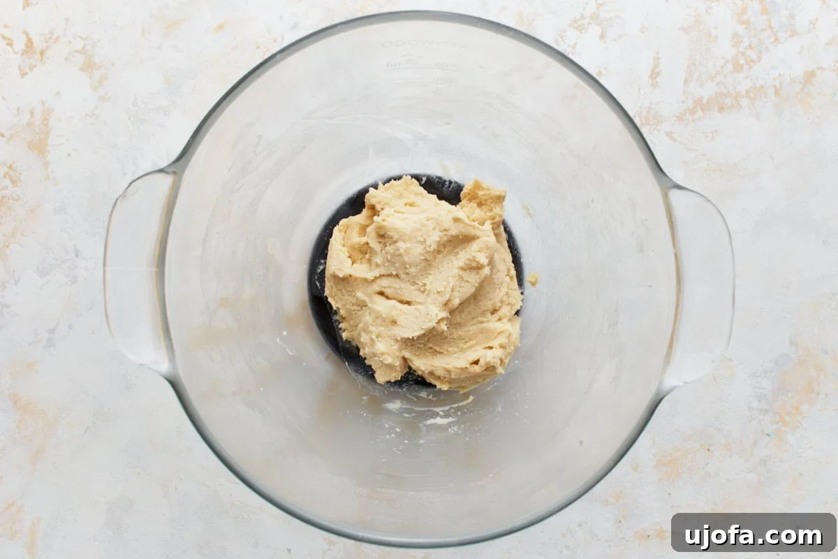 Thick and sticky gluten-free pie crust dough forming in a glass mixing bowl with a paddle attachment.
