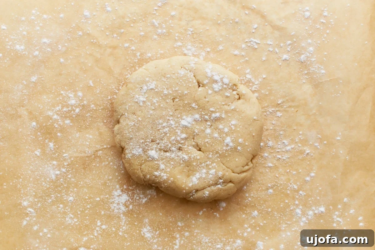 A disc of gluten-free pie crust dough on parchment paper, lightly dusted with gluten-free flour, with a rolling pin beside it.