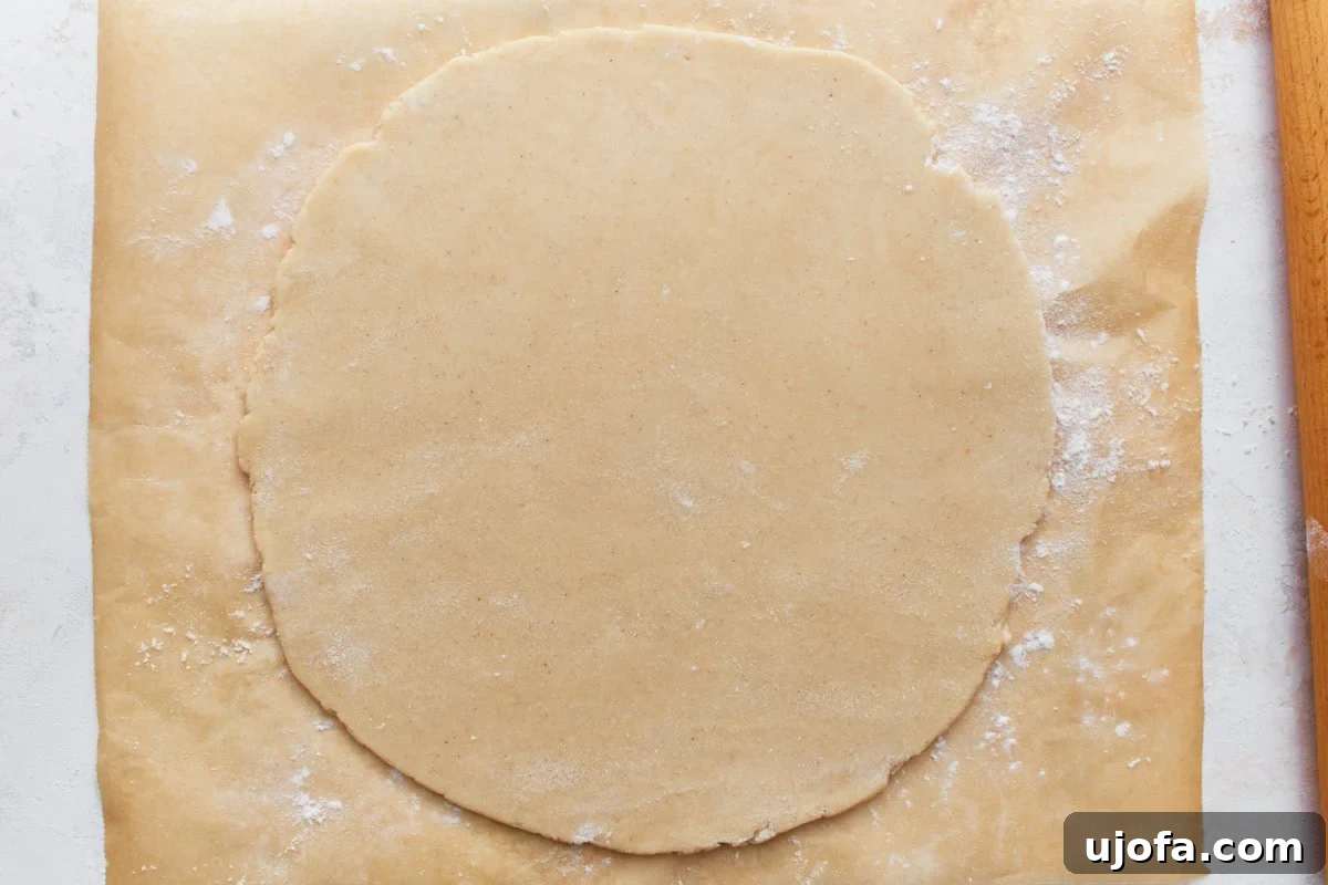 A perfectly rolled-out gluten-free pie crust on a floured parchment paper surface, ready to be transferred to a pie pan.