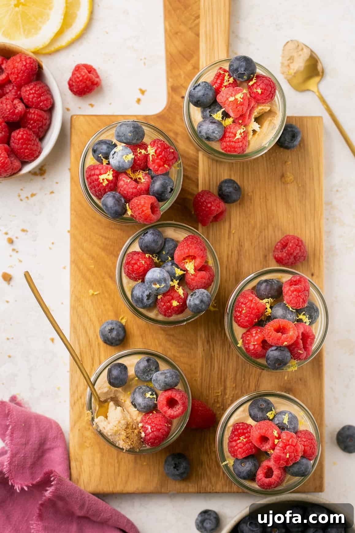 Decadent Gluten-Free No-Bake Cheesecake Cups 6 jars of no bake mini cheesecakes arranged on a wooden cutting board with a small spoon