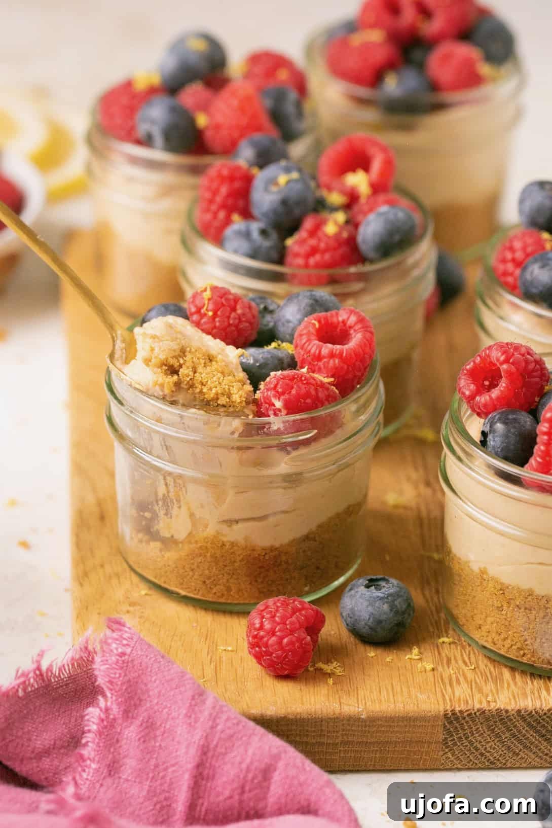 Decadent Gluten-Free No-Bake Cheesecake Cups 7 a close up photo of a no bake mini cheesecake in a jar with a golden spoon scooping out a bite, showing the creamy texture and crust layers