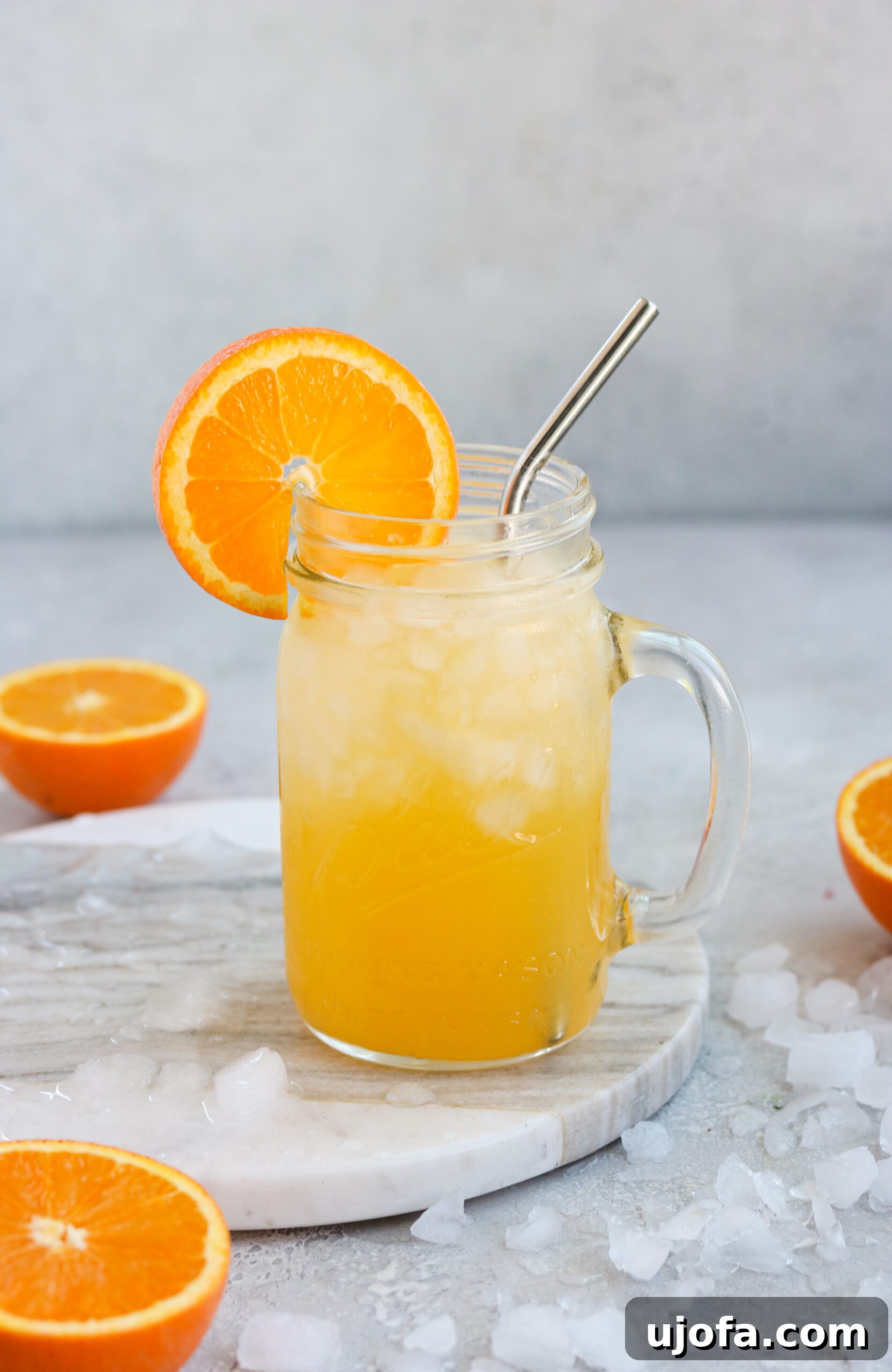 a glass of orange cocktail surrounded by ice and sliced oranges