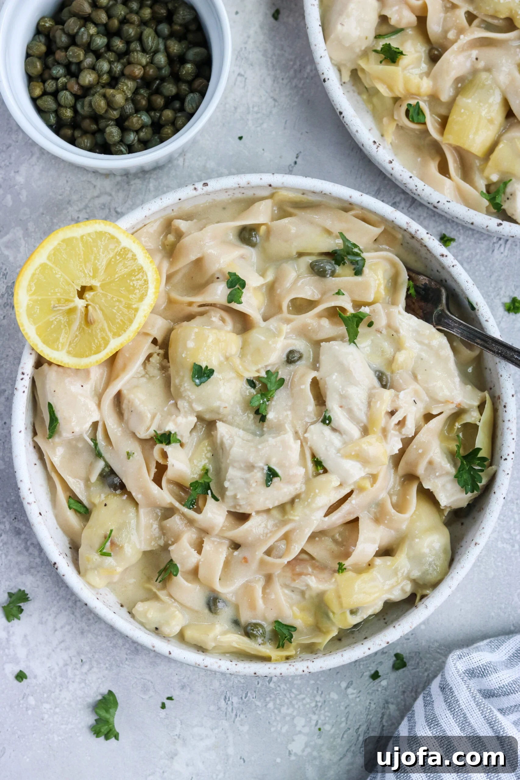 Creamy Lemon Artichoke Chicken Pasta served with fresh lemon slices and parsley garnish