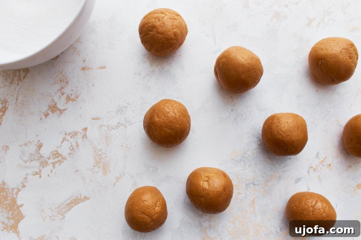 Evenly spaced gluten-free peanut butter dough balls on a flat surface, with a bowl of sugar nearby for coating.