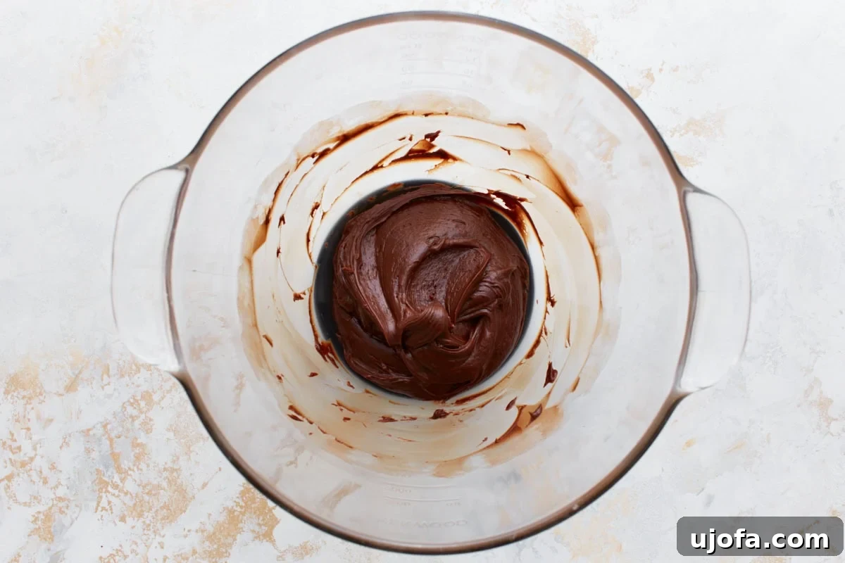 A mixing bowl containing a rich, glossy chocolate mixture with swirls, prepared for cookie filling.