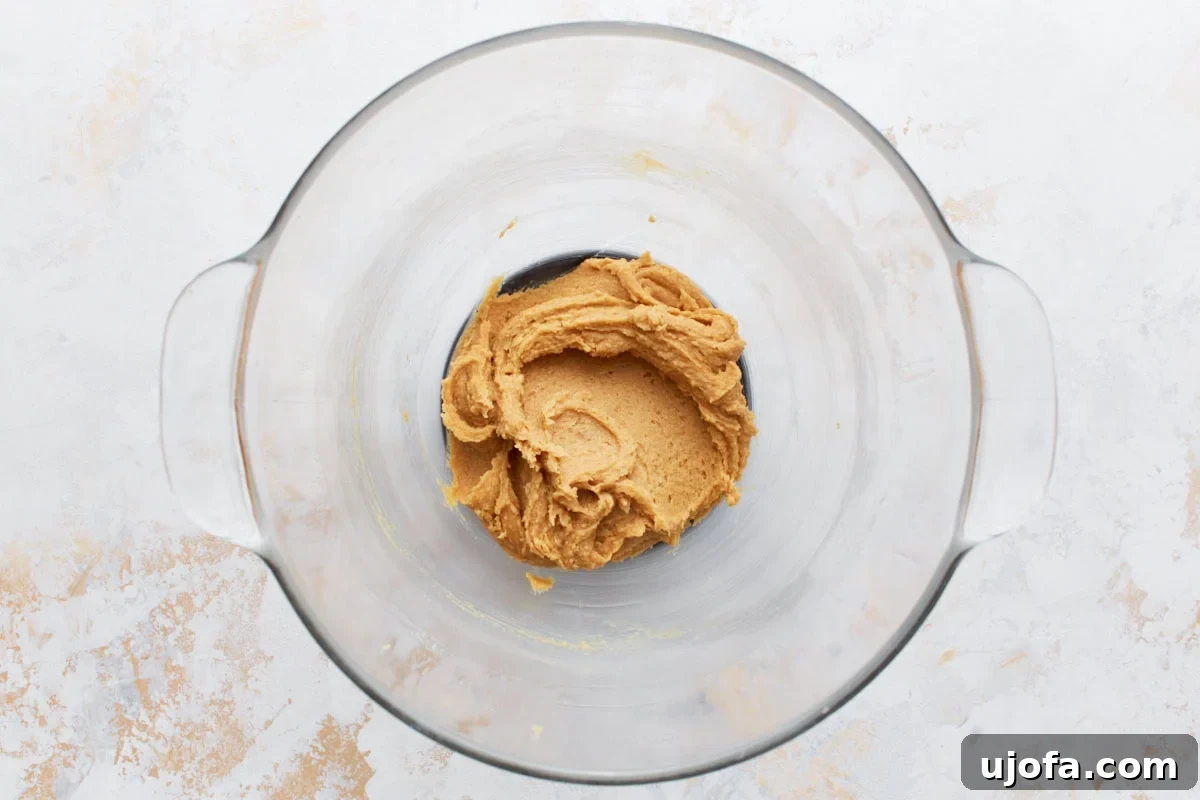 A clear mixing bowl containing creamy peanut butter dough with a smooth texture.
