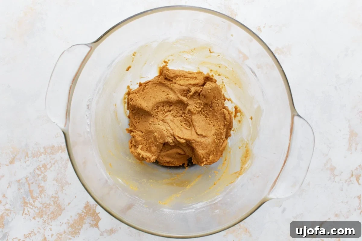 A glass mixing bowl with thick peanut butter cookie dough, ready for shaping.