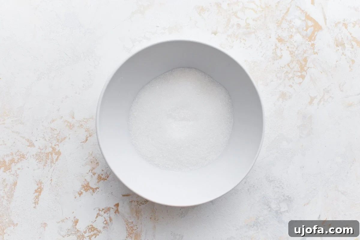 A white bowl filled with fine granulated sugar, placed on a light marbled background.