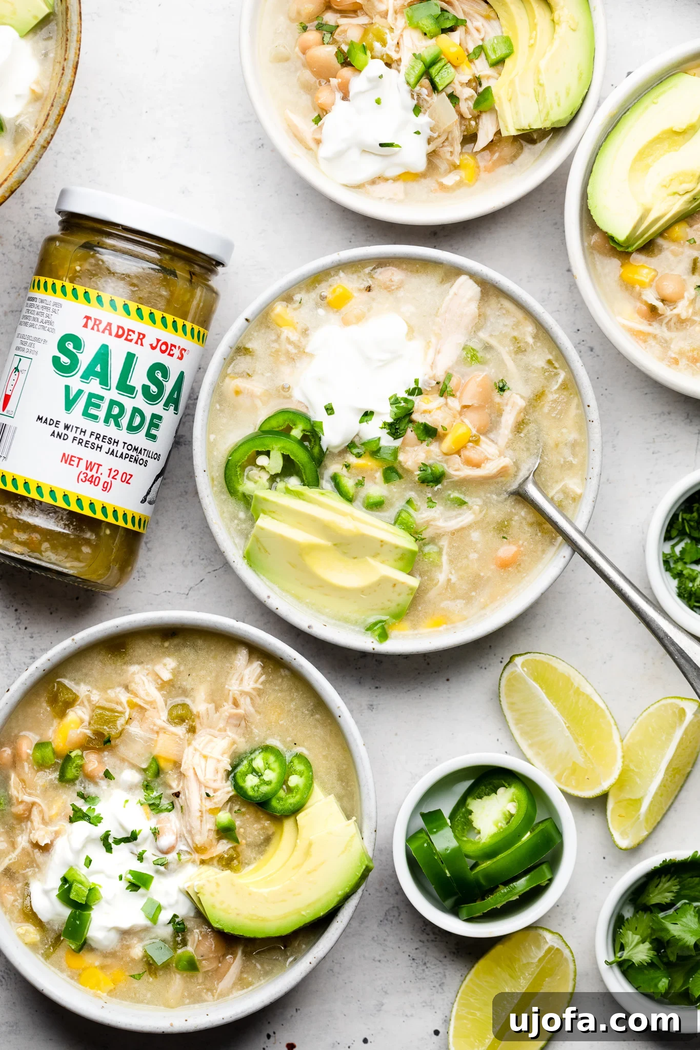 Effortless Velvety Green Chicken Chili Soup 2 Two bowls of green chicken chili soup topped with avocado and sour cream, with a jar of salsa verde nearby.