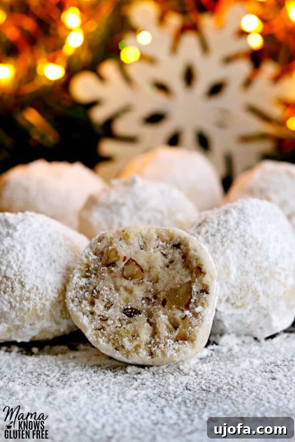 a gluten-free snowball cookie cut in half to show the texture with more cookies and a snowflake and lighted tree in the background