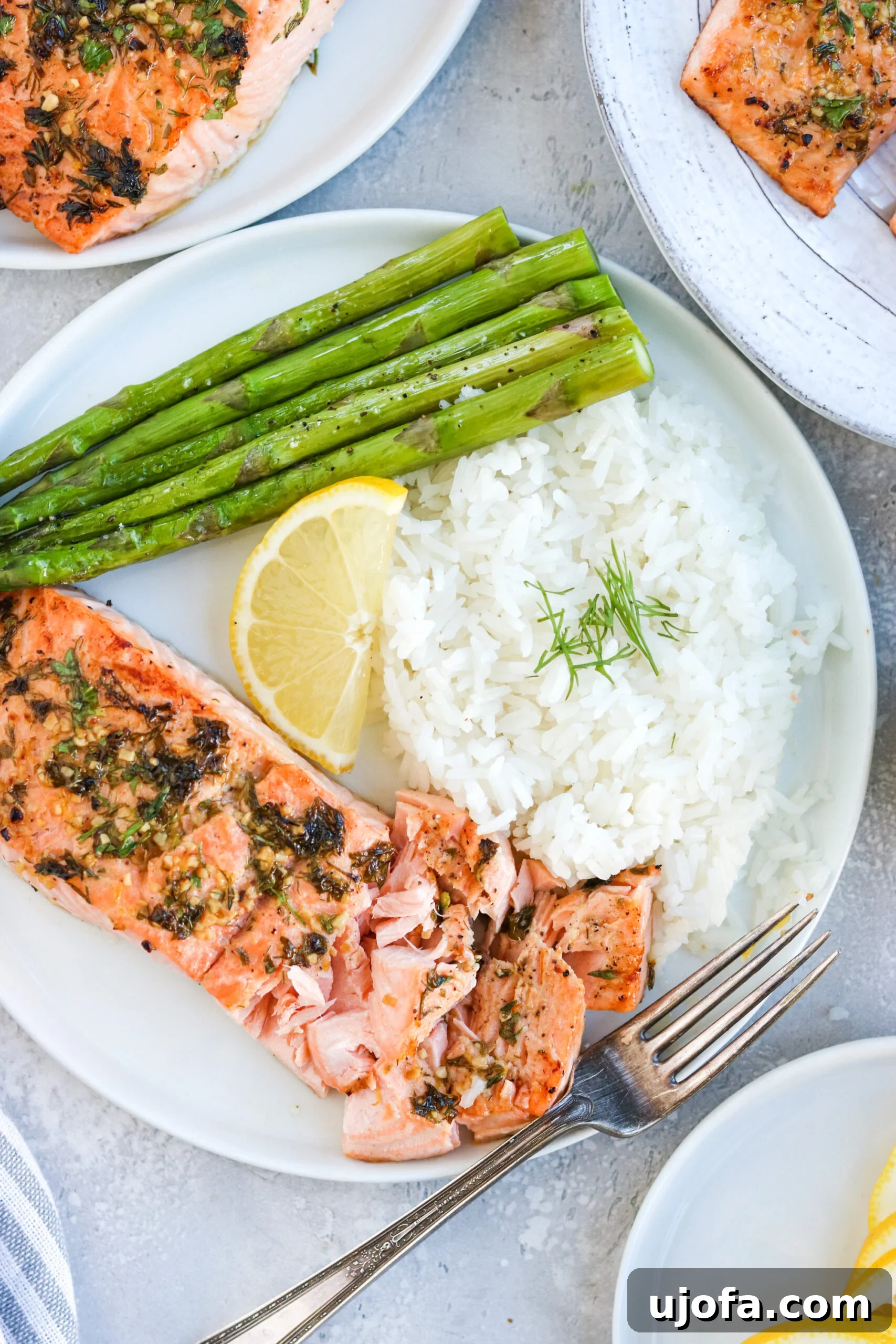 Plated Garlic Herb Baked Salmon Garlic herb baked salmon served on a white plate with tender asparagus, fluffy white rice, and a fresh lemon wedge, set against a clean white background.
