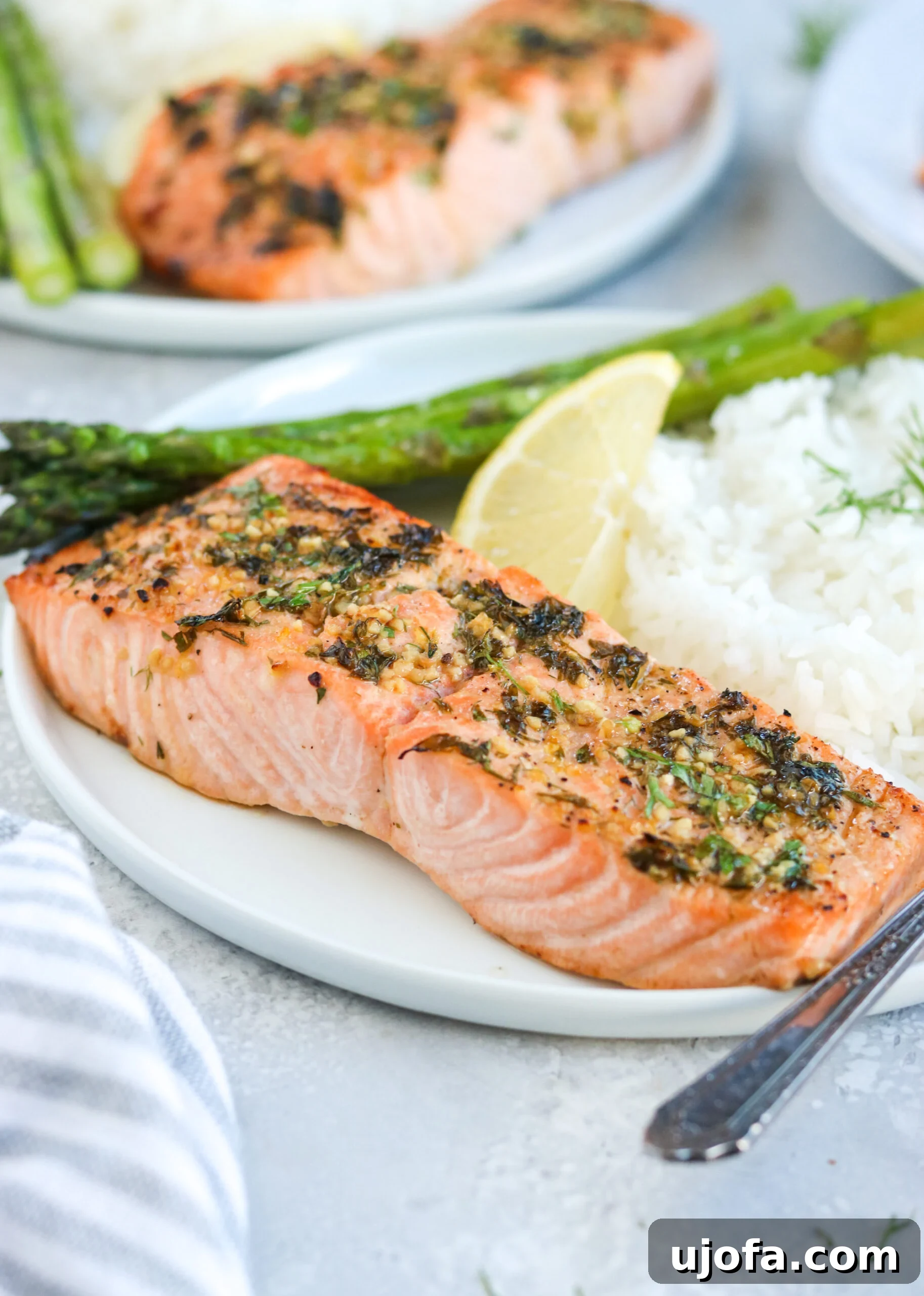 Close-up Garlic Herb Salmon Side view of a serving of garlic herb baked salmon on a white plate with asparagus, white rice, and a lemon wedge, highlighting the flakey texture.