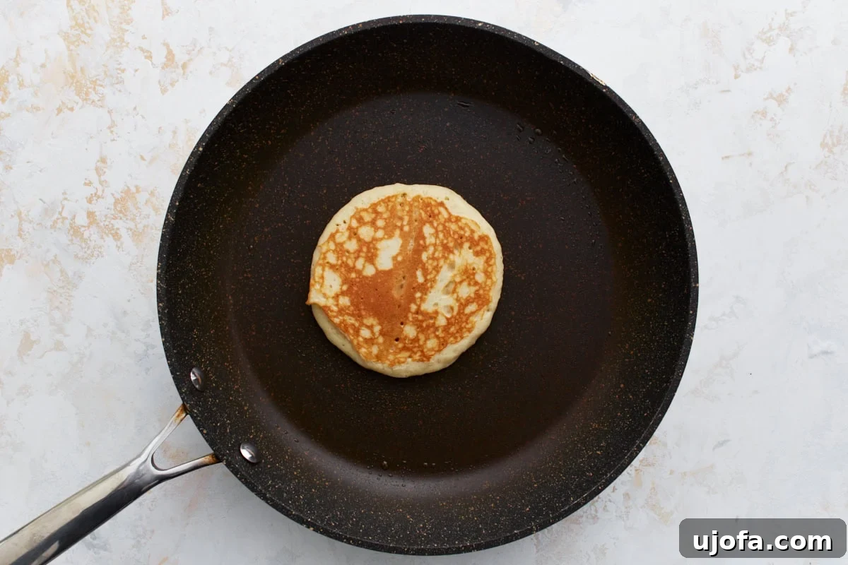 Foolproof Gluten-Free Pancakes 10 A golden-brown pancake after being flipped, cooking evenly on a black non-stick pan.