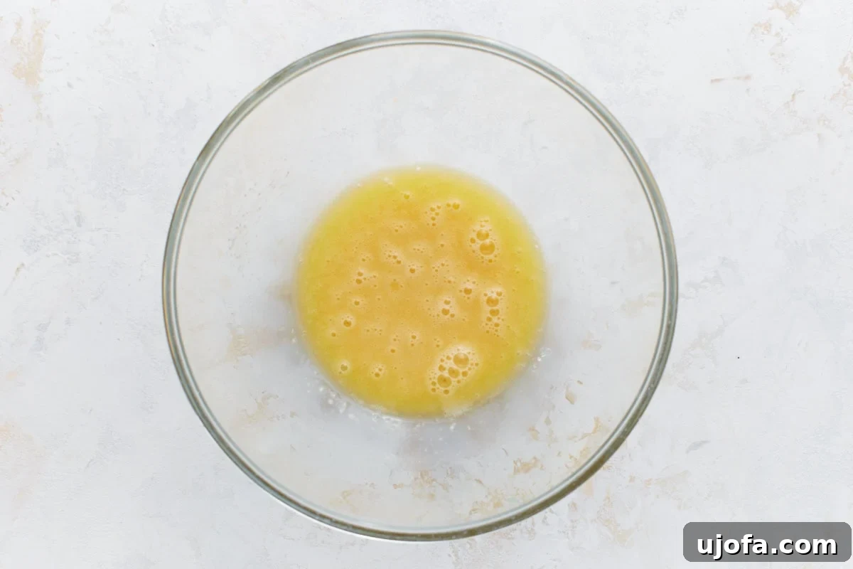 Foolproof Gluten-Free Pancakes 5 A glass mixing bowl filled with whisked eggs, showing a frothy, golden liquid against a light, textured background.