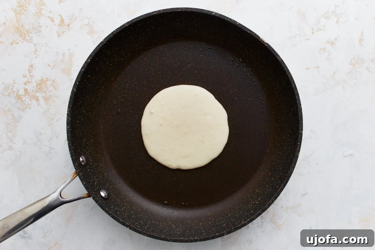 Foolproof Gluten-Free Pancakes 8 A single pancake cooking on a greased, non-stick skillet, with a slightly uneven shape.