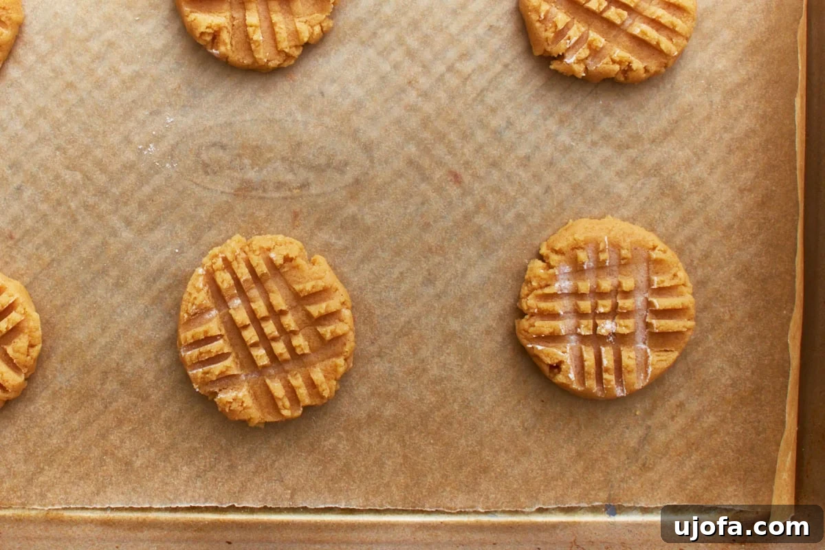 Gluten-free peanut butter cookies with distinct fork crosshatch patterns on a parchment-lined baking sheet, ready for the oven.