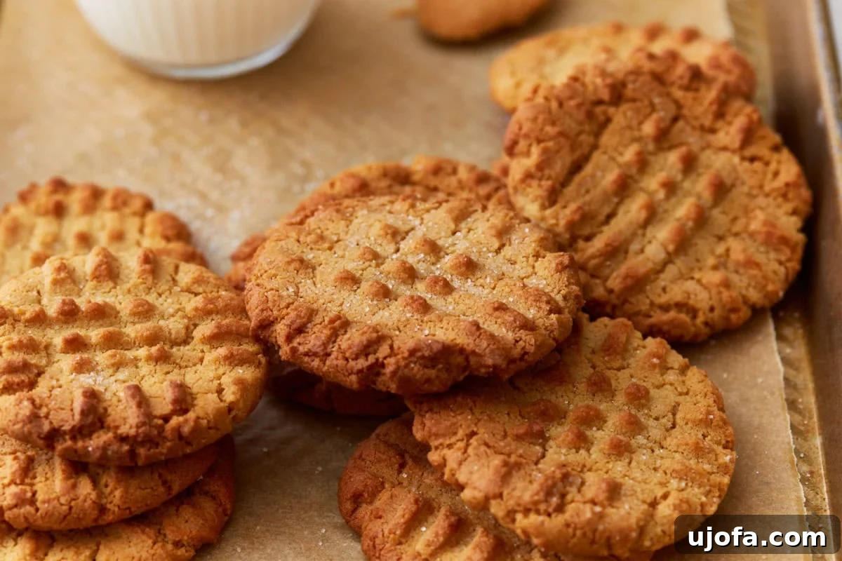 Freshly baked gluten-free peanut butter cookies stacked on parchment paper, with a refreshing glass of milk in the background, ready to be enjoyed.