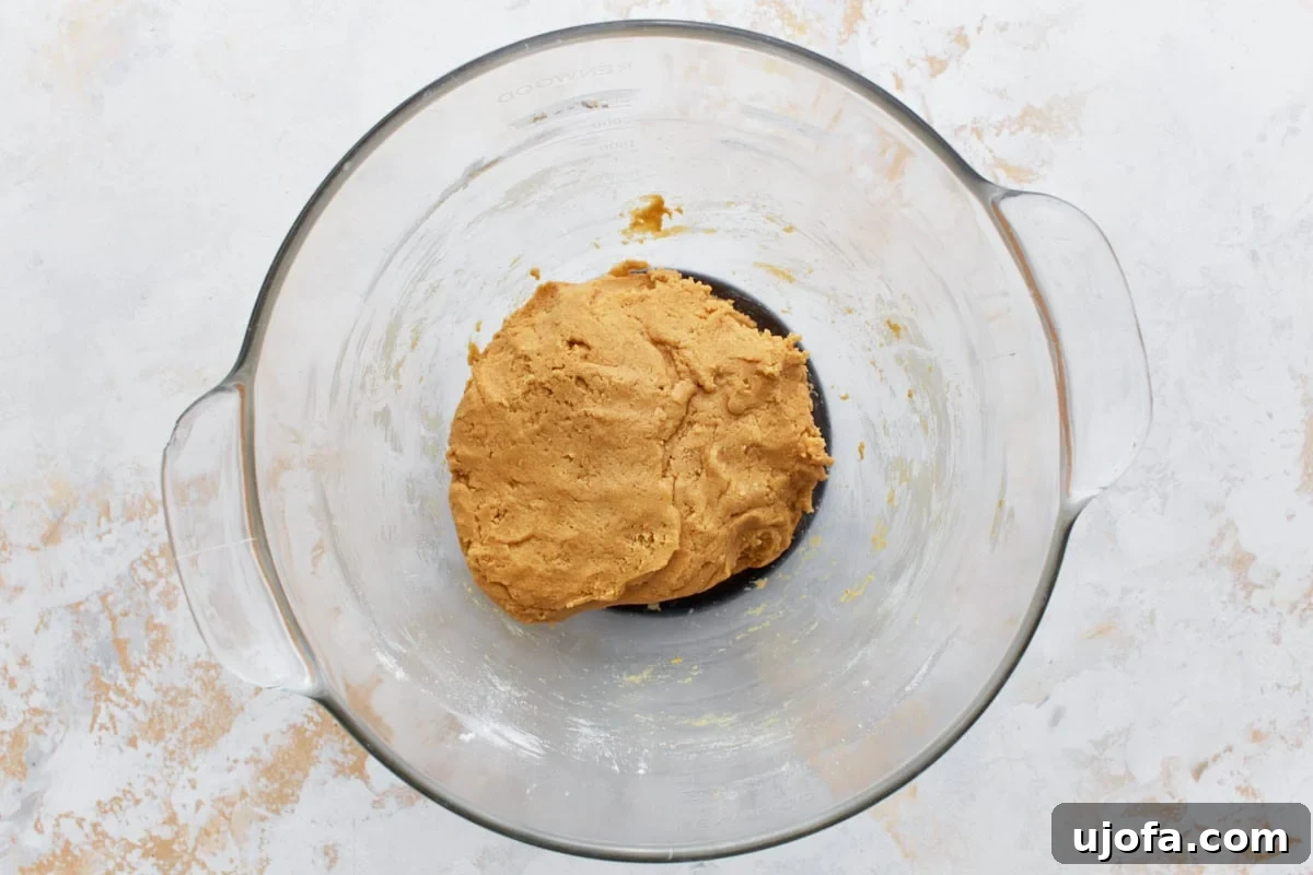 Smooth, soft gluten-free peanut butter cookie dough in a glass bowl on a light surface, freshly mixed.