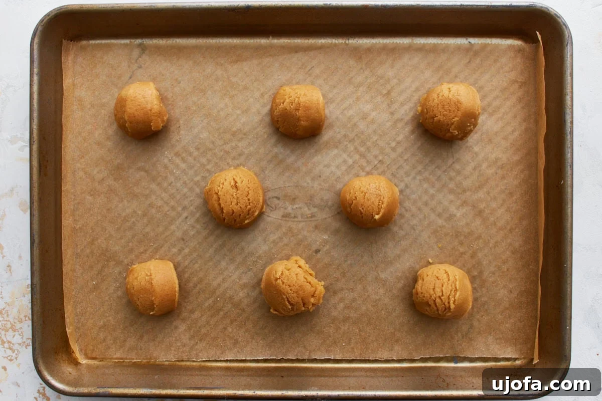 Eight evenly scooped gluten-free peanut butter cookie dough balls neatly arranged on a parchment-lined baking sheet.