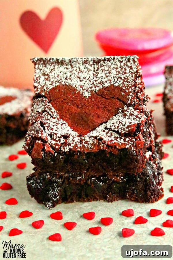 Gluten-Free Dairy-Free Red Velvet Brownies 2 2 gluten-free red velvet brownies stacked on top of each other with more brownies, a heart cup and heart candy in the background