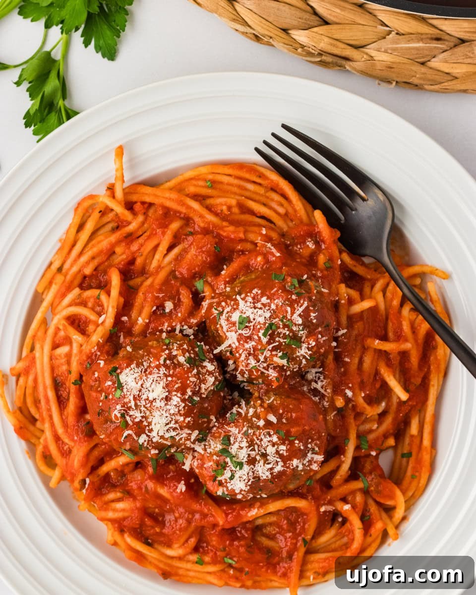 Three baked gluten-free meatballs served over spaghetti with marinara sauce, topped with grated Parmesan and fresh parsley.