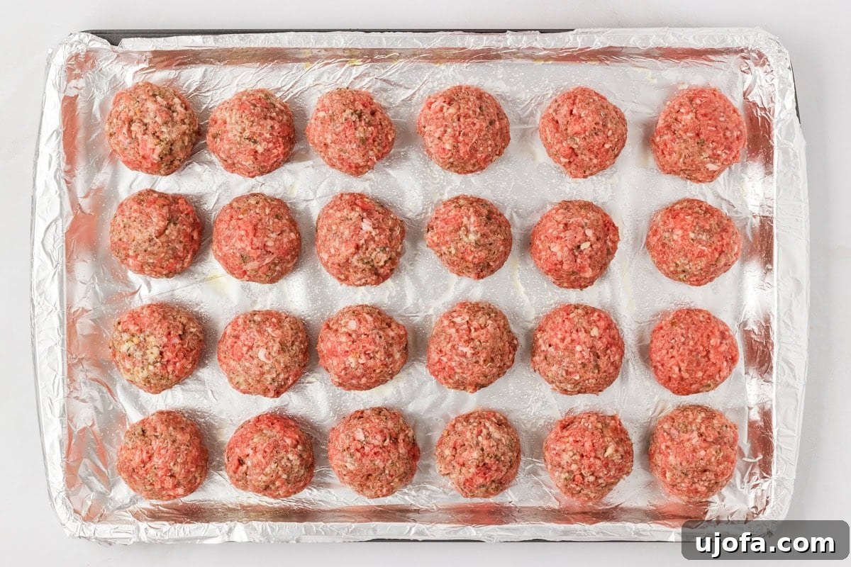 Evenly spaced raw gluten-free meatballs lined up on a foil-covered baking sheet, ready to go into the oven.