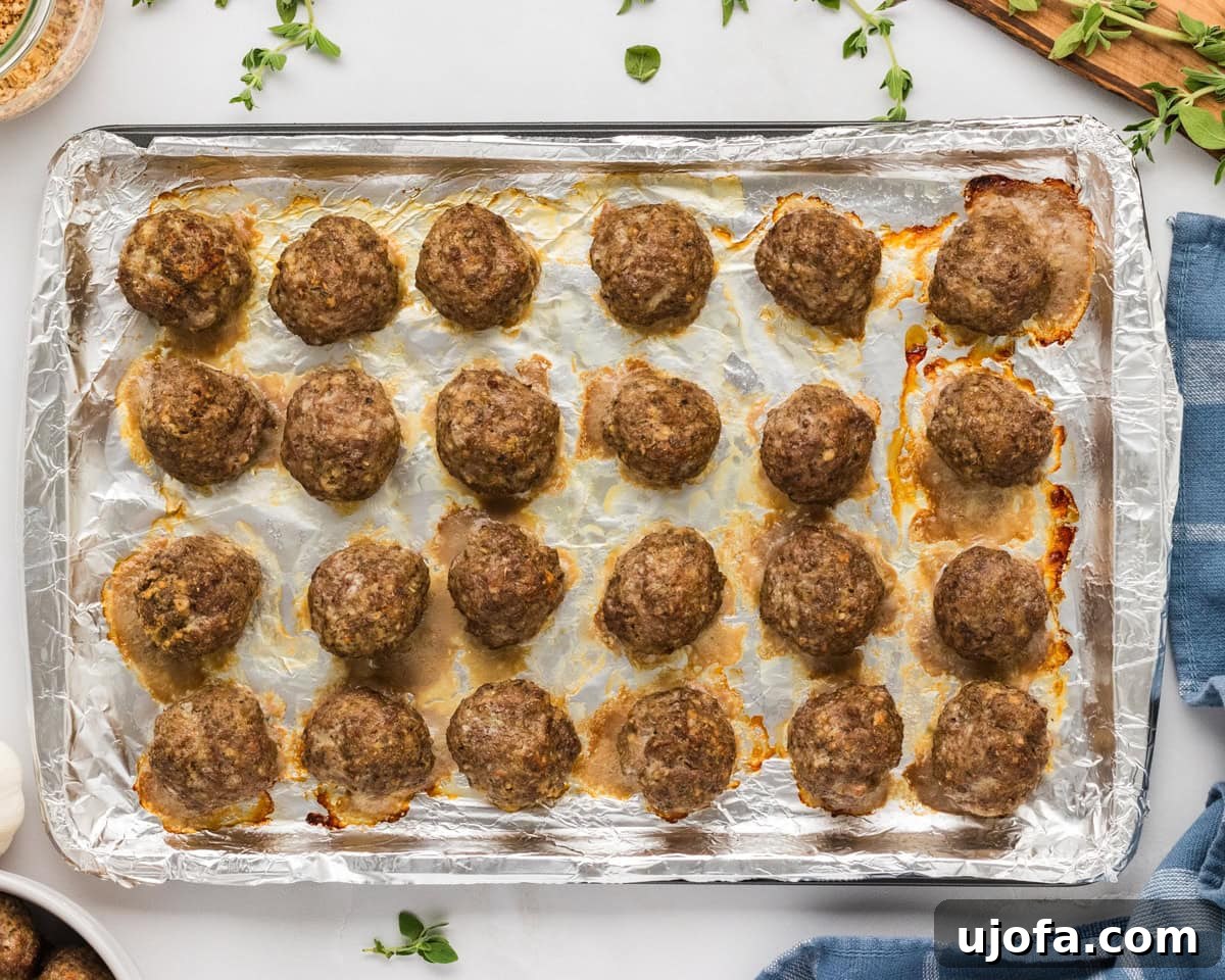 Freshly baked gluten-free meatballs on a foil-lined sheet pan, golden and cooked through.