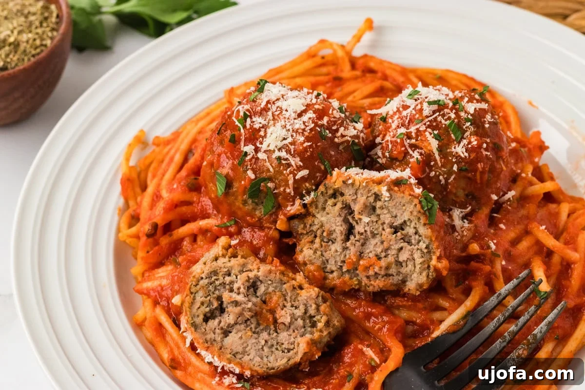 A plate of spaghetti topped with marinara sauce and three gluten-free meatballs, one cut open to show the juicy, tender center. Sprinkled with grated Parmesan and chopped parsley.