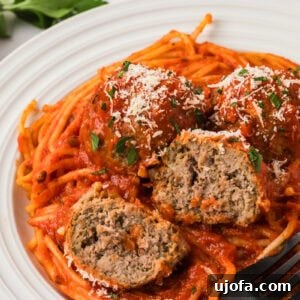 A plate of spaghetti topped with marinara sauce and three gluten-free meatballs, one cut open to show the juicy, tender center. Sprinkled with grated Parmesan and chopped parsley.