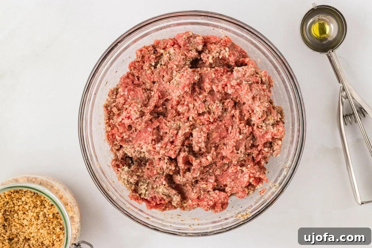 Ground beef mixed with gluten-free breadcrumb mixture in a glass bowl, ready to shape into meatballs.
