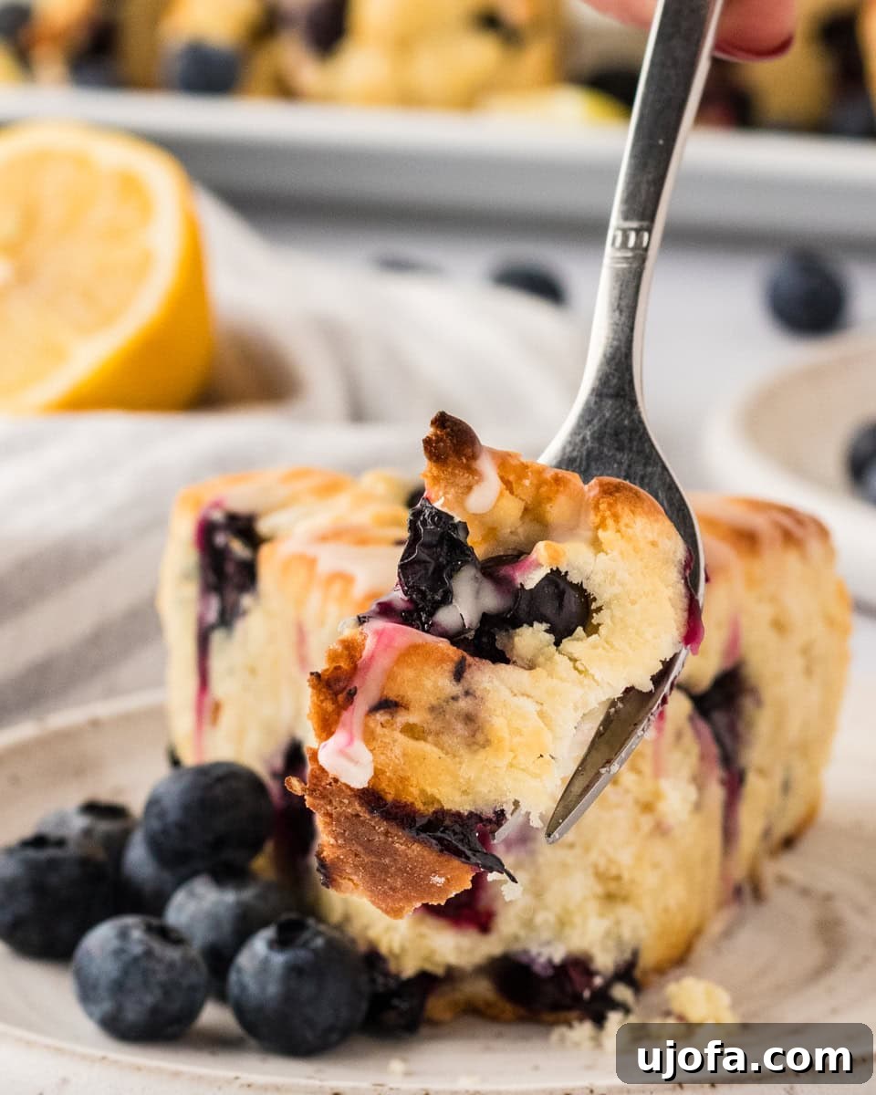 Blueberry Burst Gluten-Free Scones 20 A plate with a slice of a gluten-free blueberry scone, a fork holding a bite-sized piece, surrounded by fresh blueberries and a hint of lemon in the background.