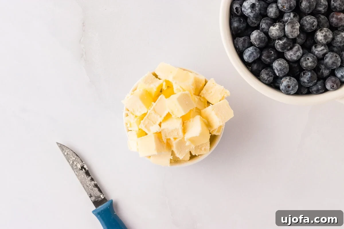 Blueberry Burst Gluten-Free Scones 5 Small bowls filled with cubed butter and fresh blueberries, next to a small paring knife on a white marble surface.
