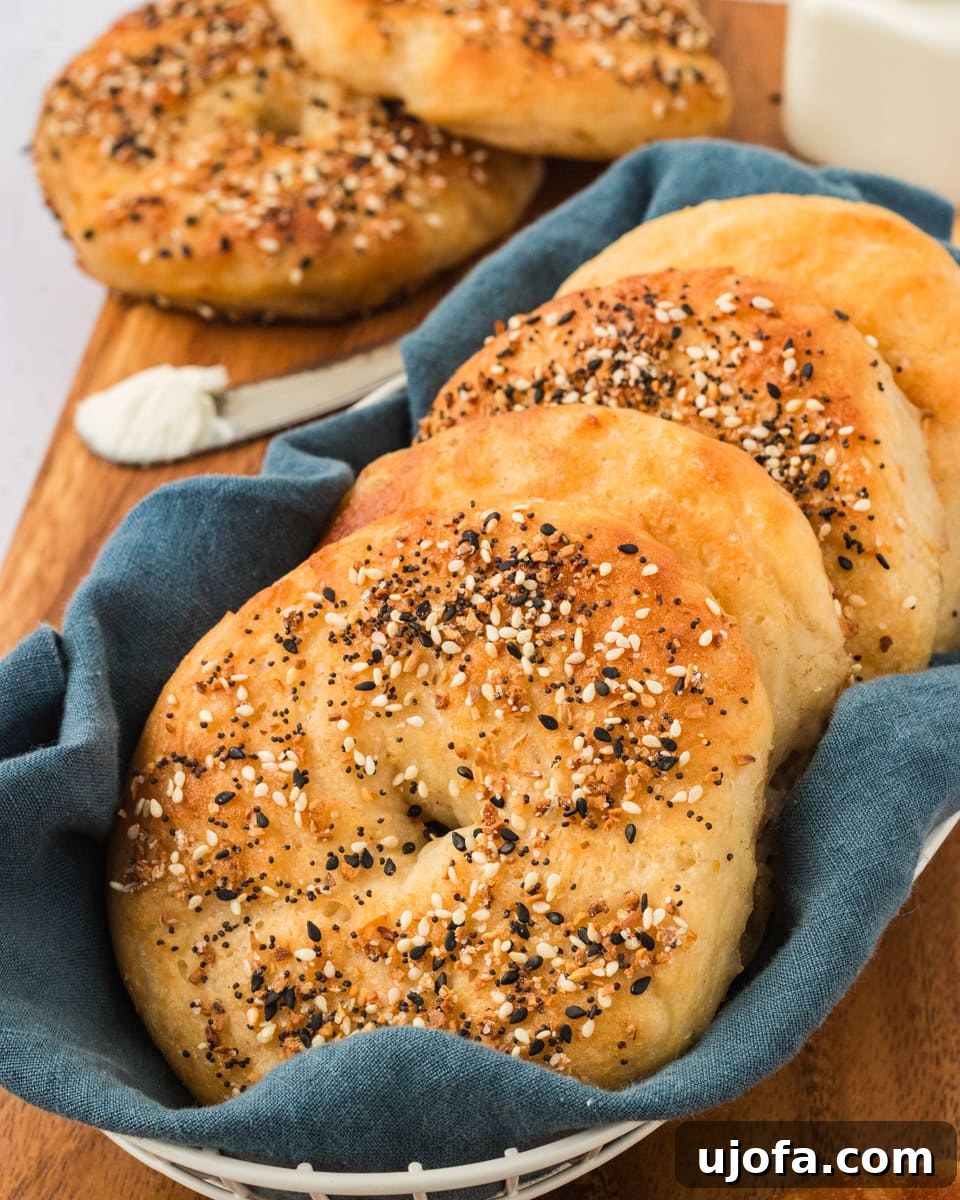 Golden brown gluten-free everything bagels arranged in a white basket lined with a blue cloth, served on a wooden board with a spread of cream cheese.